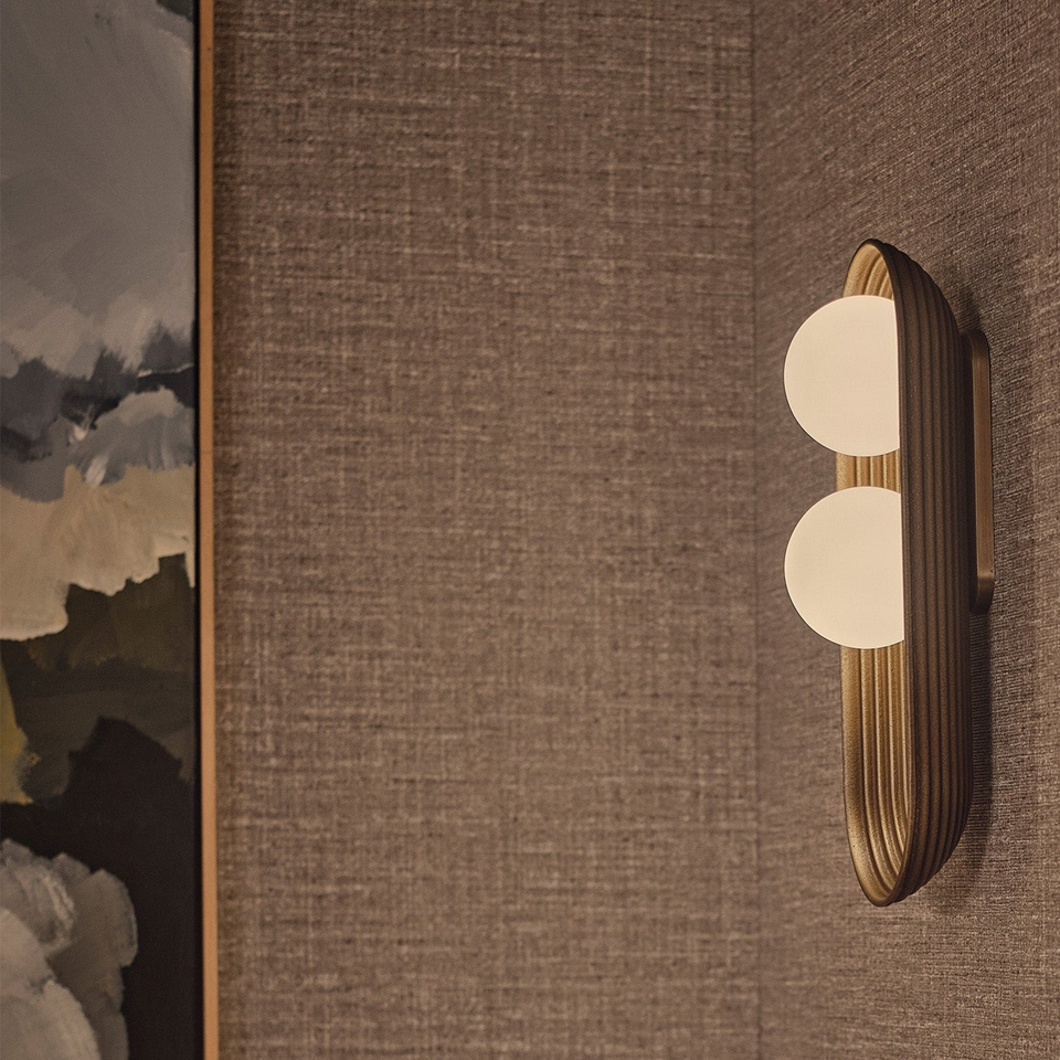 Twin Oval Wall Light – Reeded Wood & Opal Glass, Matt Gold or Bronze | Jagmag Lights 3 Matt-gold twin oval wall light mounted on a textured grasscloth wall beside framed artwork
