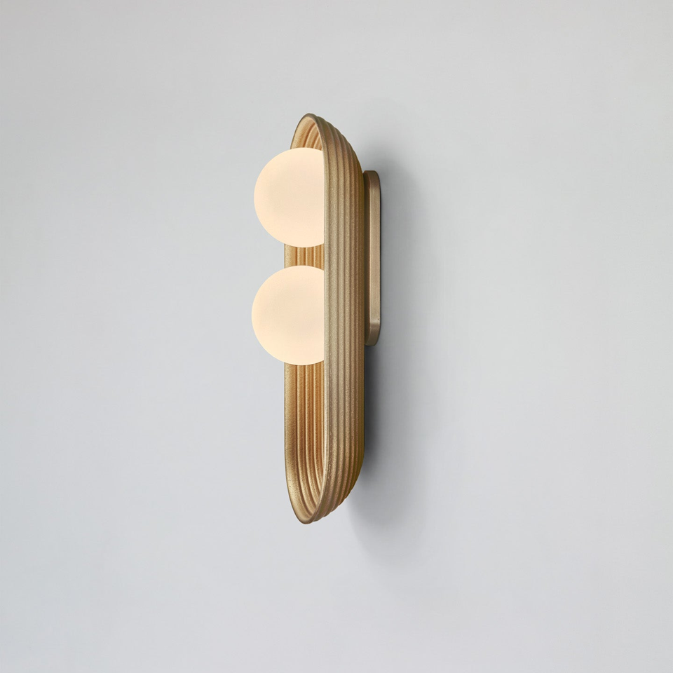 Twin oval wall light in matt gold, reeded wood capsule backplate with two opal glass balls, on a grey wall