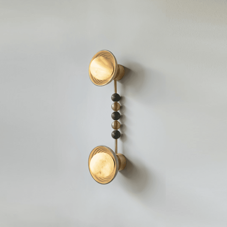 Home 2 Twin wall sconce with two reeded matt-gold wood bowls and opal glass balls lit, joined by a stem of gold-metal and green stone beads, on a plain wall