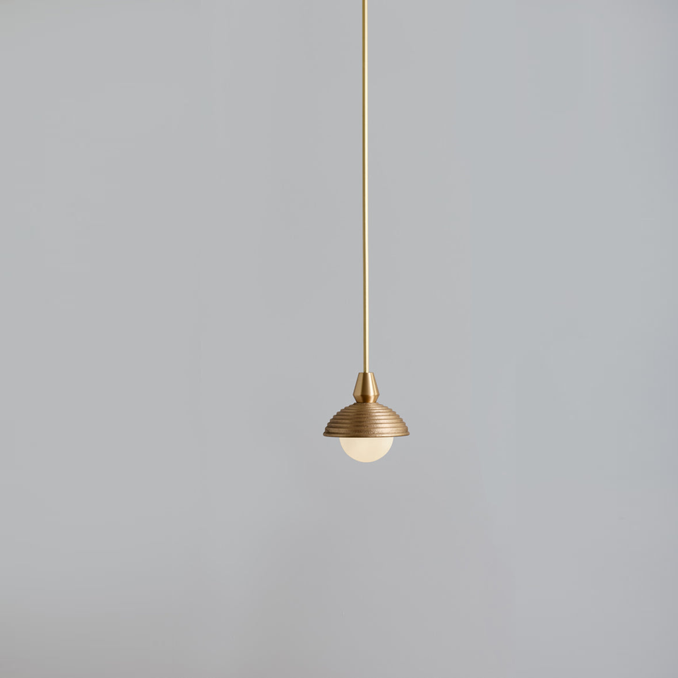 Wood pendant light with a reeded matt-gold dome and opal glass ball on a brass cord, on a grey wall