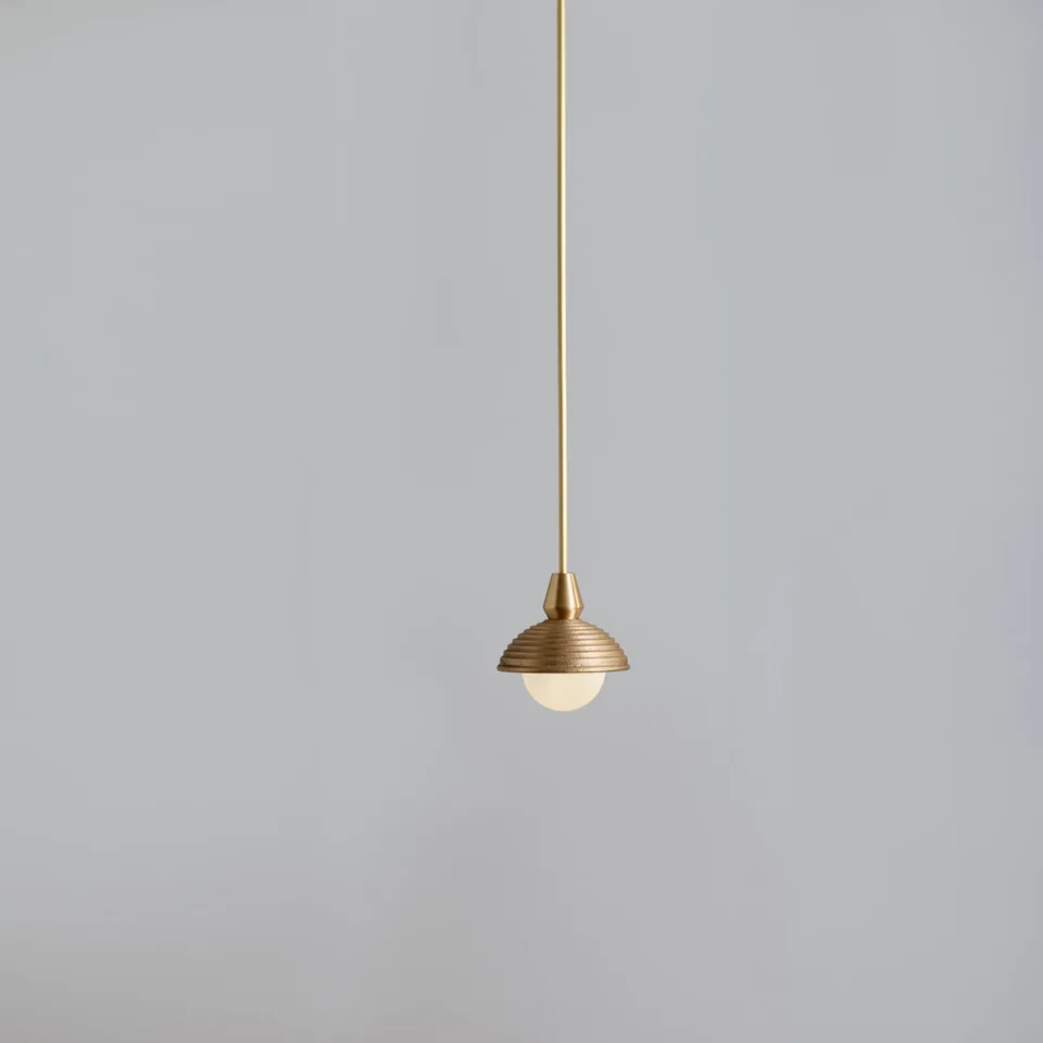 Wood pendant light with a reeded matt-gold dome and opal glass ball on a brass cord, on a grey wall