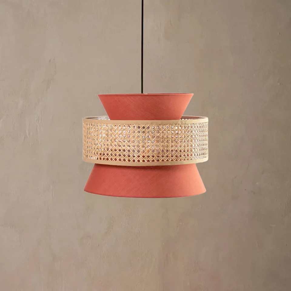 Terracotta cane and fabric layered drum pendant light on a plaster wall, a woven cane band between two rust-orange fabric cones