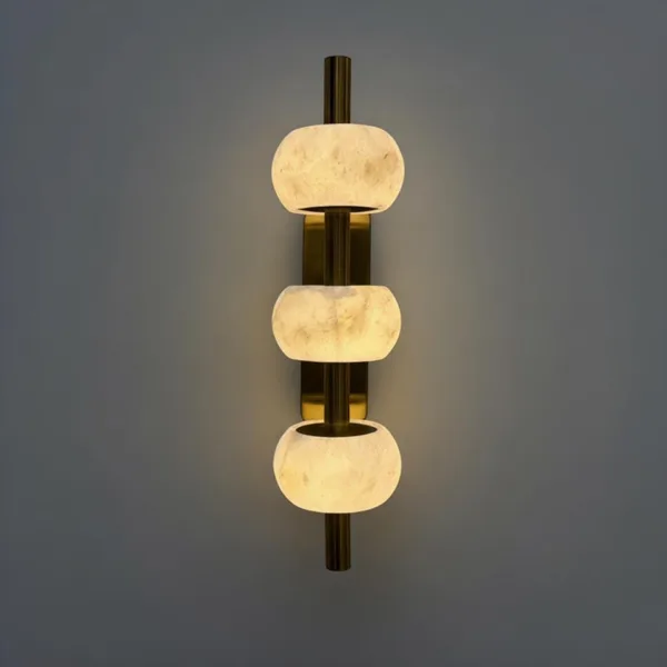 Three lit alabaster beads stacked on a slim brass-finish wall light