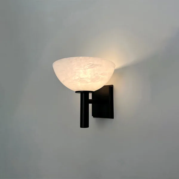 Alabaster bowl wall light glowing against a pale grey wall, light spreading upward from the open stone bowl
