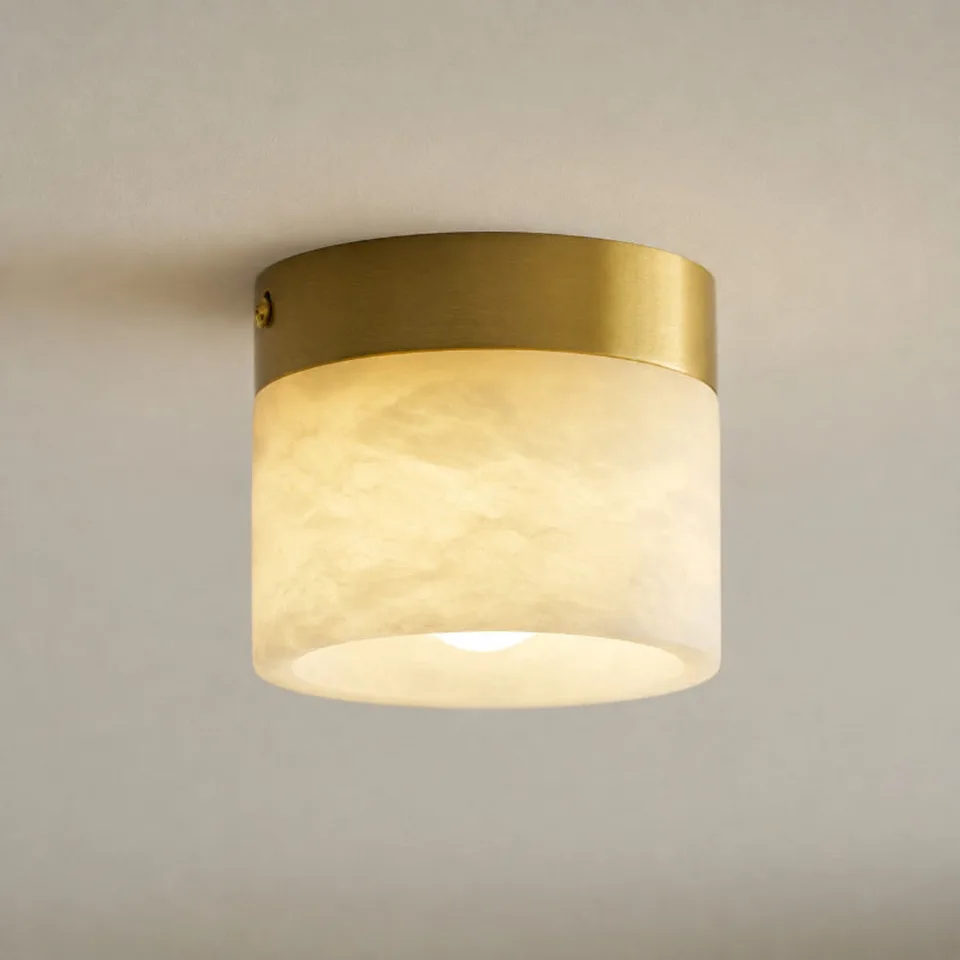 Cylinder ceiling light in natural alabaster glowing warm under a brass-finish canopy