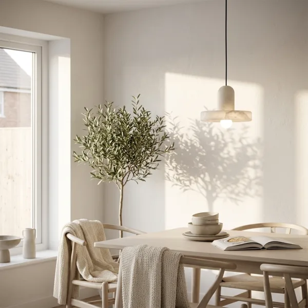 Alabaster disc pendant light over a light wood dining table beside an olive tree