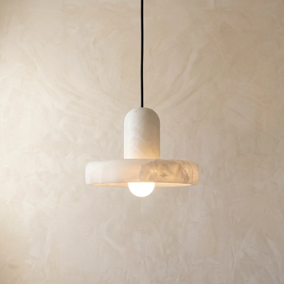 Natural alabaster disc pendant light with an opal globe bulb glowing against a plaster wall