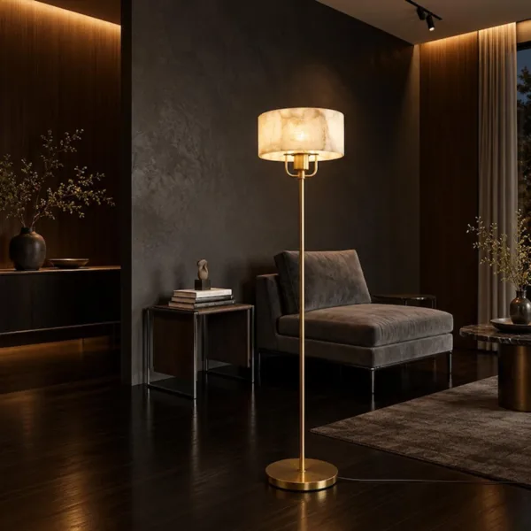 Lit alabaster drum floor lamp in a dark lounge beside a grey chaise