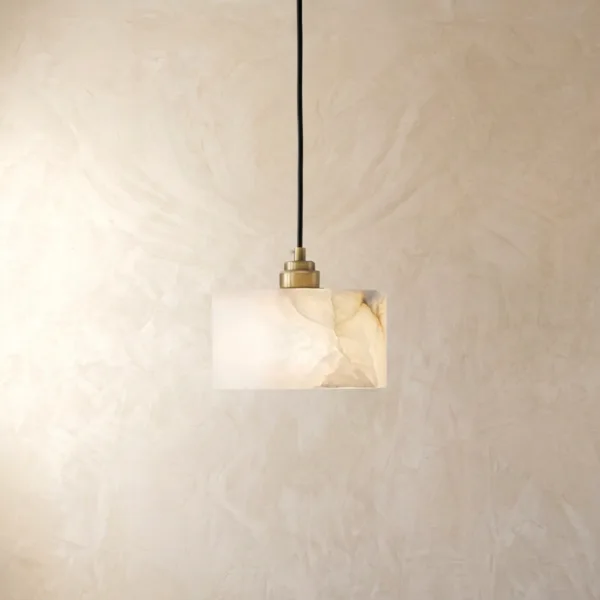 Natural alabaster drum pendant light with a brass socket cup glowing against a plaster wall, showing soft white veining