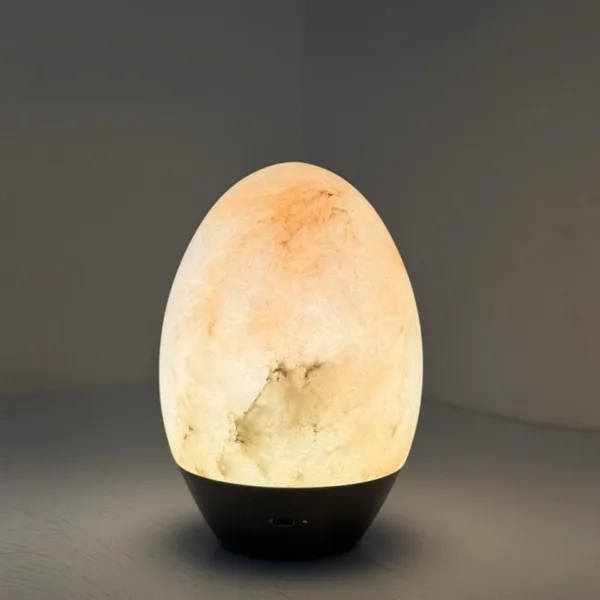 Lit alabaster egg lamp on its black base in the evening