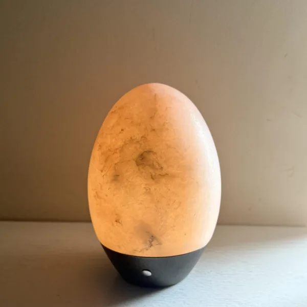 Glowing alabaster egg night lamp on a black base with its button