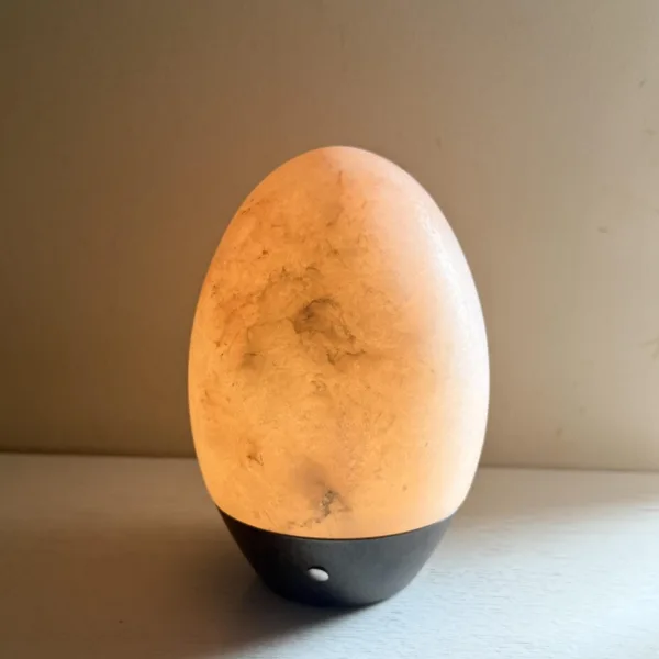 Alabaster egg table lamp glowing warm on a white shelf