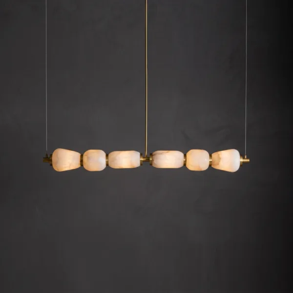 Kitchen island chandelier with six lit alabaster shades on a brass bar, dark wall