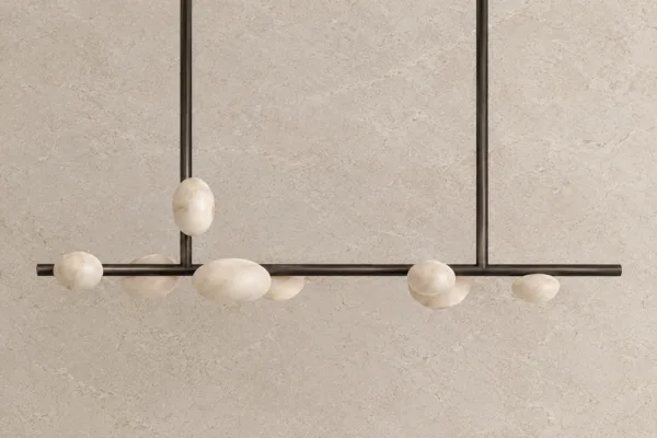 G9 alabaster pebble linear chandelier with organic stone diffusers on a bronze bar, unlit, against a stone wall