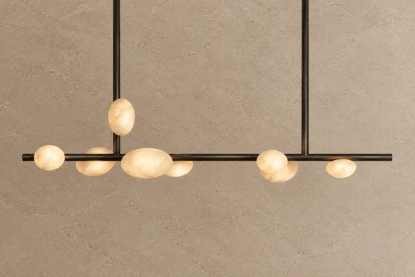 Lit alabaster pebble linear chandelier hanging in front of a stone wall