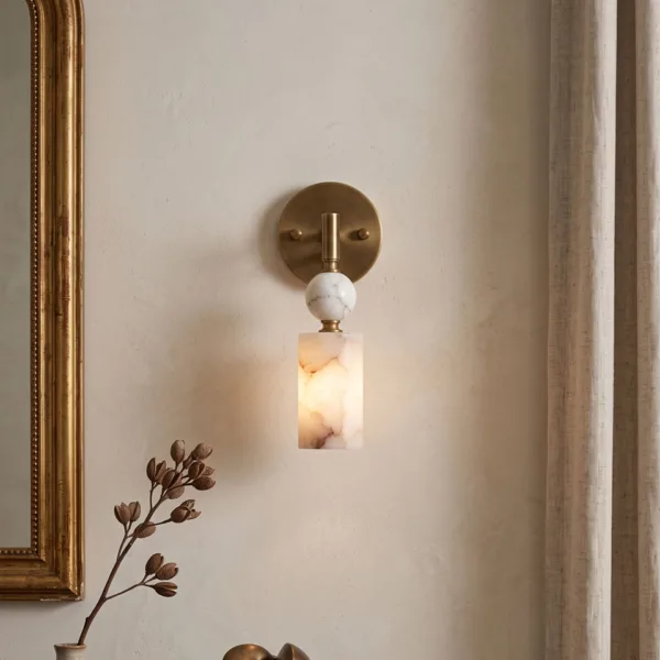 Alabaster pendant wall light beside a gilt mirror and linen curtain