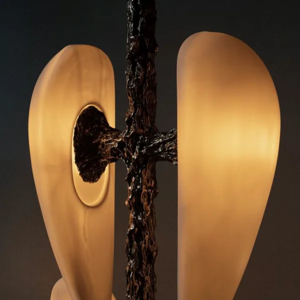 Close-up of a lit alabaster teardrop joined to the textured cast metal arm, glowing warm