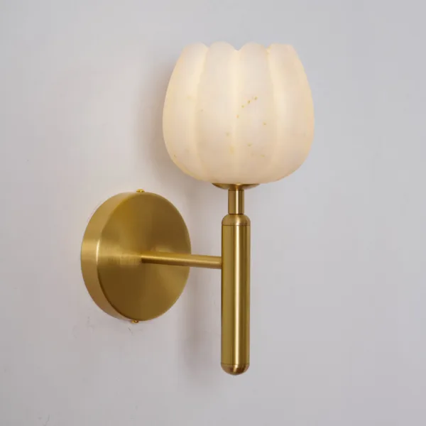 Lit alabaster tulip sconce seen from the side on a pale wall