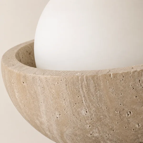 Close-up of the honed travertine bowl with its natural pits and banding around the opal globe