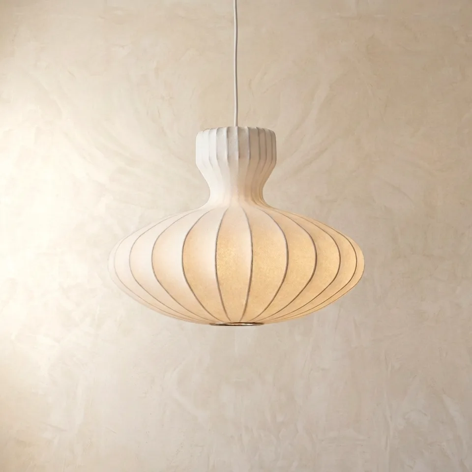 Cocoon pendant light with a white onion-dome shade glowing warm, hanging on a plaster wall