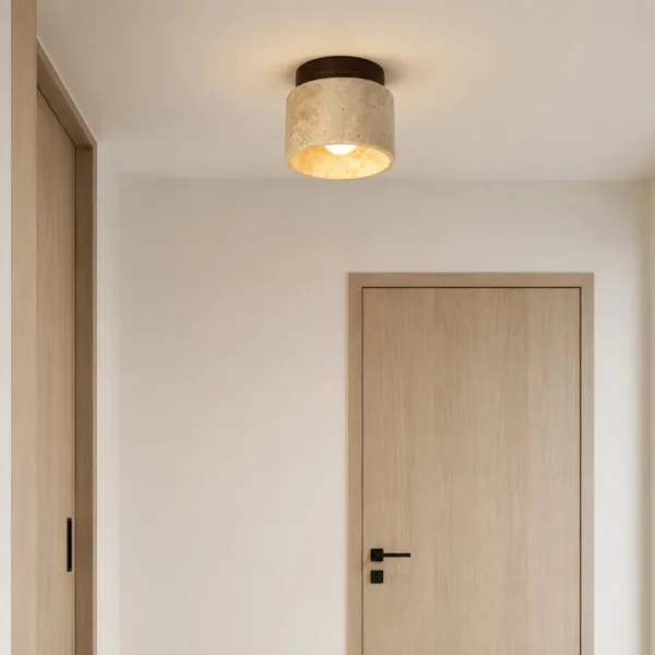 Travertine drum ceiling light glowing above a pale oak door in a white hallway