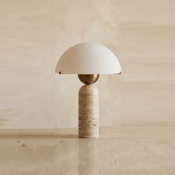 Designer table lamp with a travertine column, brass-finish ball and white opal glass dome on a cream wall