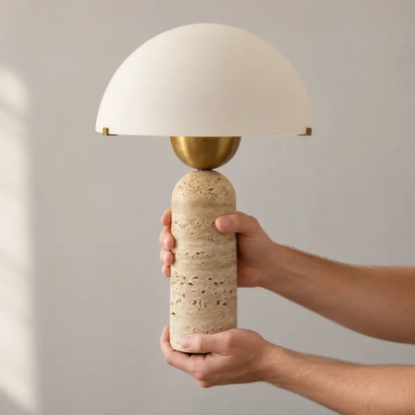 Two hands holding the travertine table lamp, showing its size against the opal glass dome