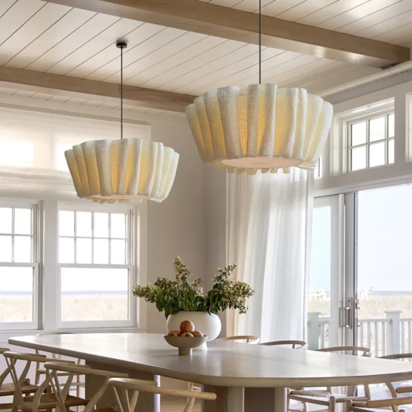 Two draped fabric pendant lights hanging over a long dining table beside seaside windows
