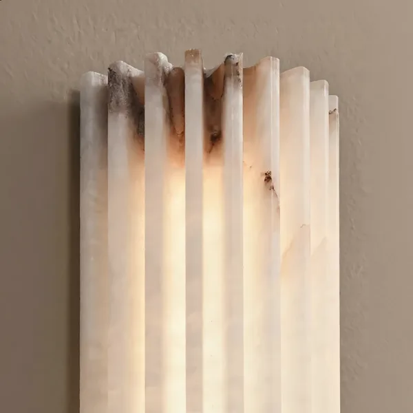 Close-up of the carved alabaster flutes and their uneven natural top edge, lit from behind