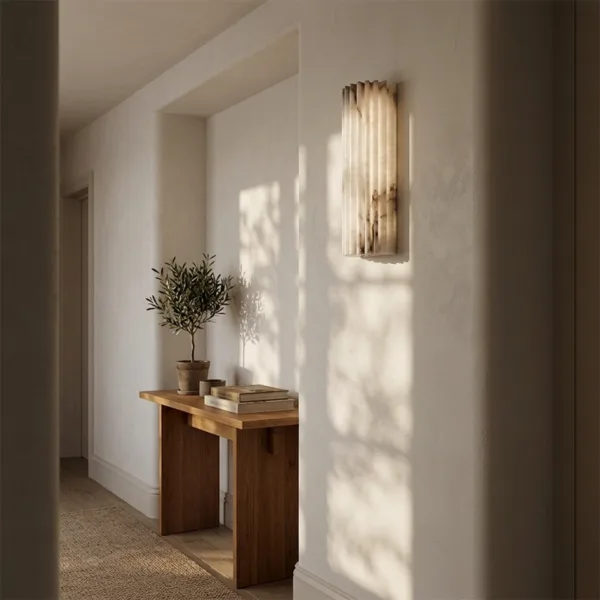 Fluted alabaster wall light above a wooden console in a sunlit hallway