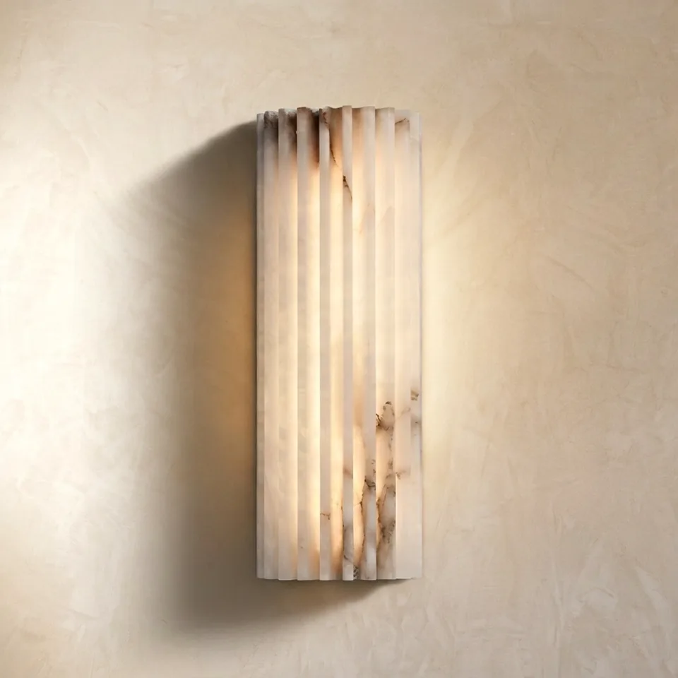 Fluted alabaster wall light glowing warm with grey-amber veining on a plaster wall