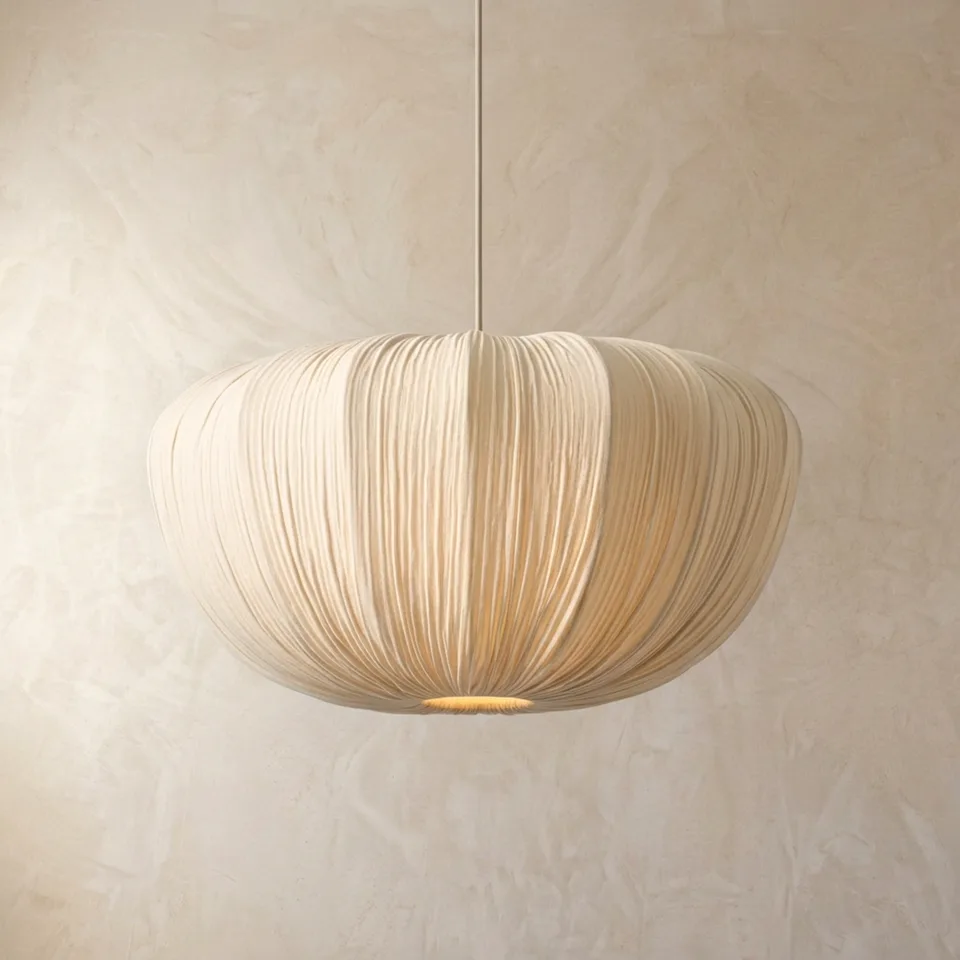 Japanese fabric cloud pendant light glowing softly with a warm light at its base against a plaster wall