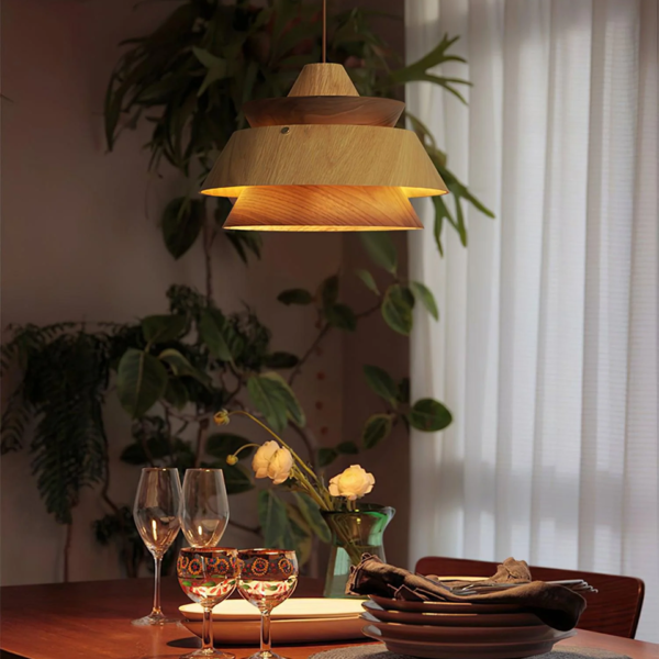 Layered wood pendant light glowing warm over a dining table set for dinner