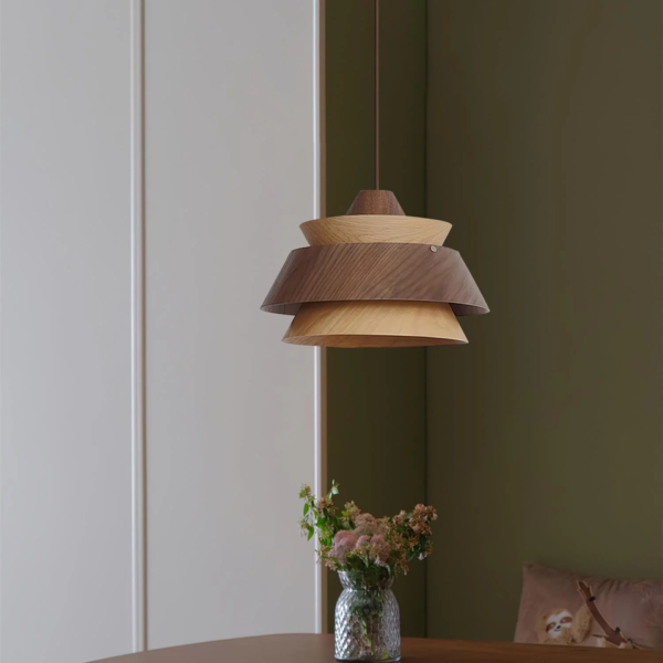 Layered wood pendant light against a dark green wall above a vase of flowers