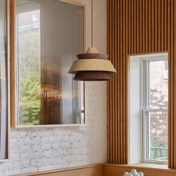 Layered wood pendant light hanging by a window beside a slatted wood wall