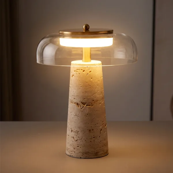 Modern LED table lamp lit warm: a travertine cone base under a clear glass dome and brass-finish LED disc