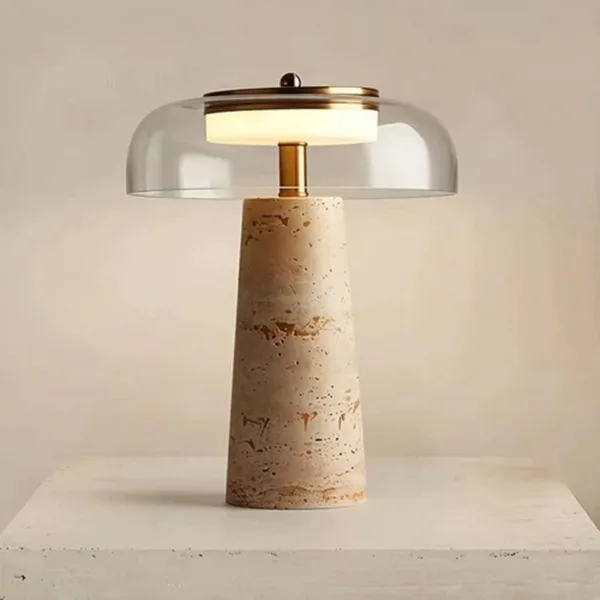 Travertine LED table lamp standing on a white stone plinth, its built-in LED glowing under the glass