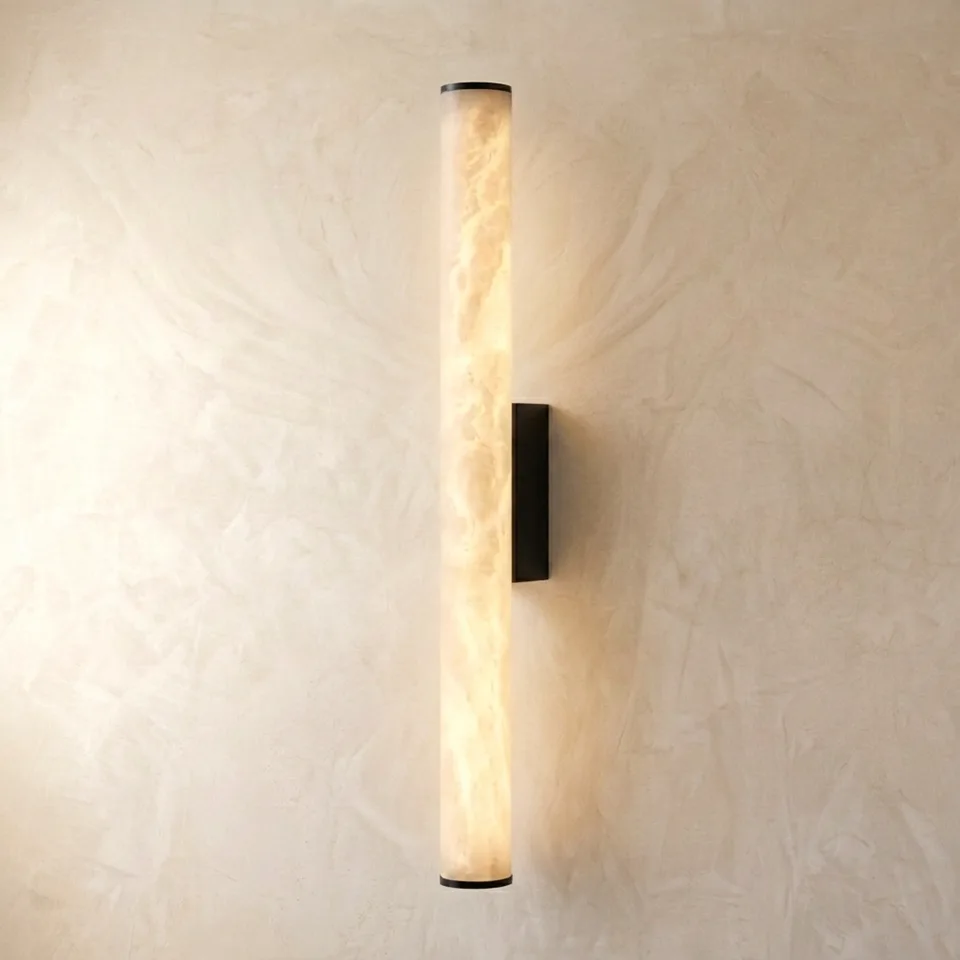 Lit alabaster tube wall light on a plaster wall showing honey veins in the stone