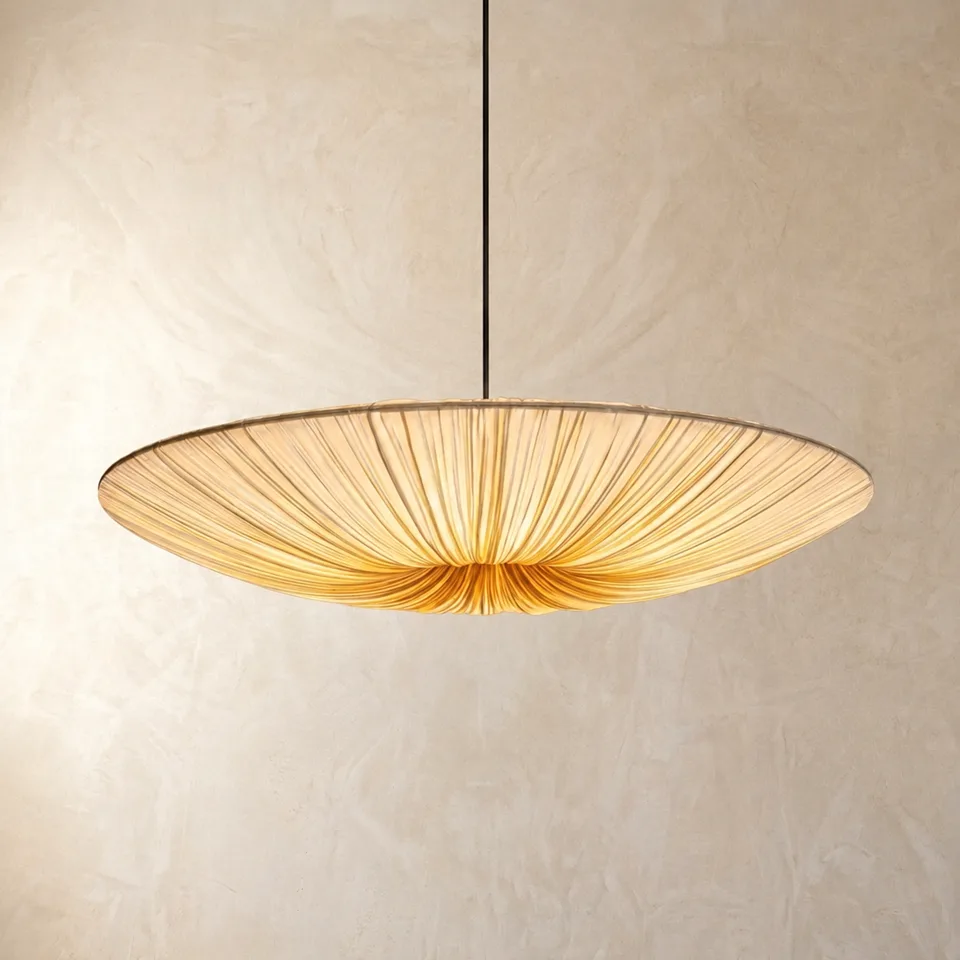 Pleated silk saucer pendant light glowing warm, hanging on a plaster wall