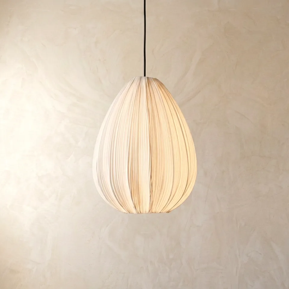 Pleated silk teardrop pendant light glowing warm, hanging on a plaster wall