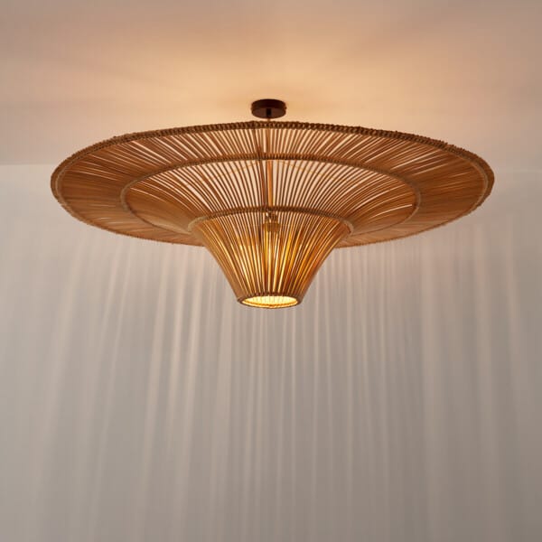 Rattan pendant lamp hung close to the ceiling, glowing through the cone with striped shadows on the wall