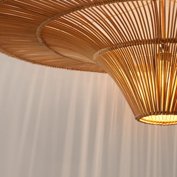 Lit central cone of the rattan pendant lamp casting rays of shadow on a white wall