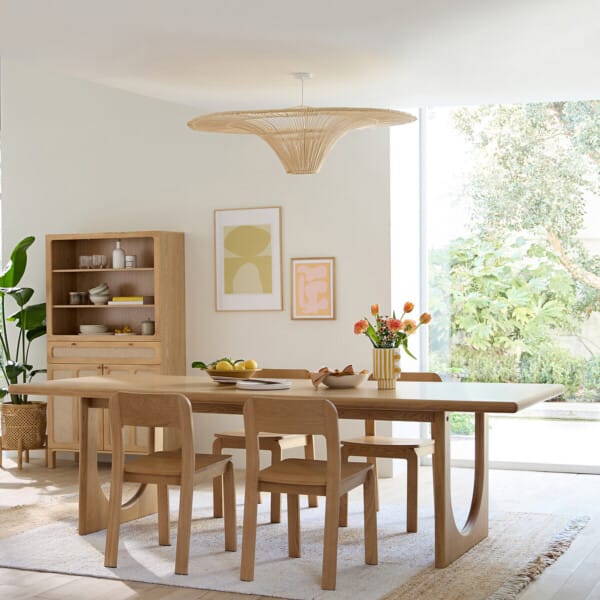 Rattan pendant lamp with a wide sunburst shade over an oak dining table in a bright dining room