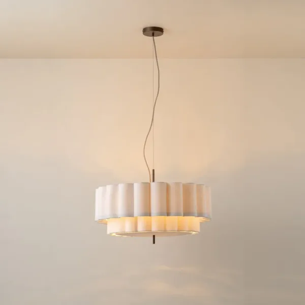 Scalloped linen drum pendant light lit warm, full view with cord, on a neutral wall