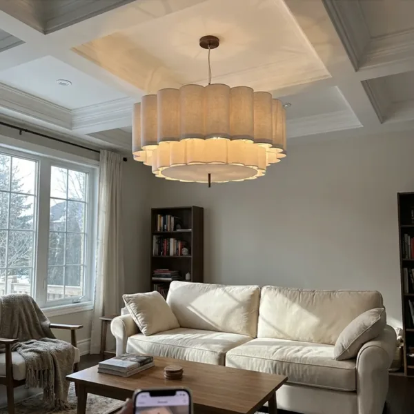 Scalloped linen drum pendant light lit in a living room with a coffered ceiling