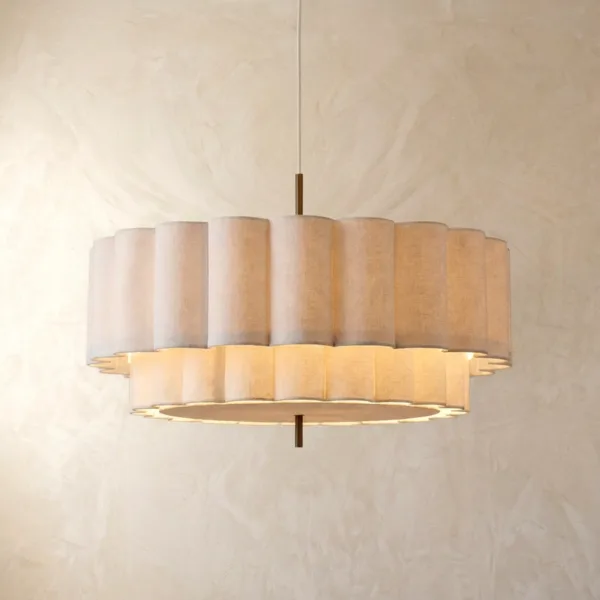 Two-tier scalloped linen drum pendant light in natural off-white, hanging on a plaster wall