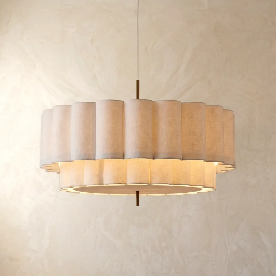 Two-tier scalloped linen drum pendant light in natural off-white, hanging on a plaster wall