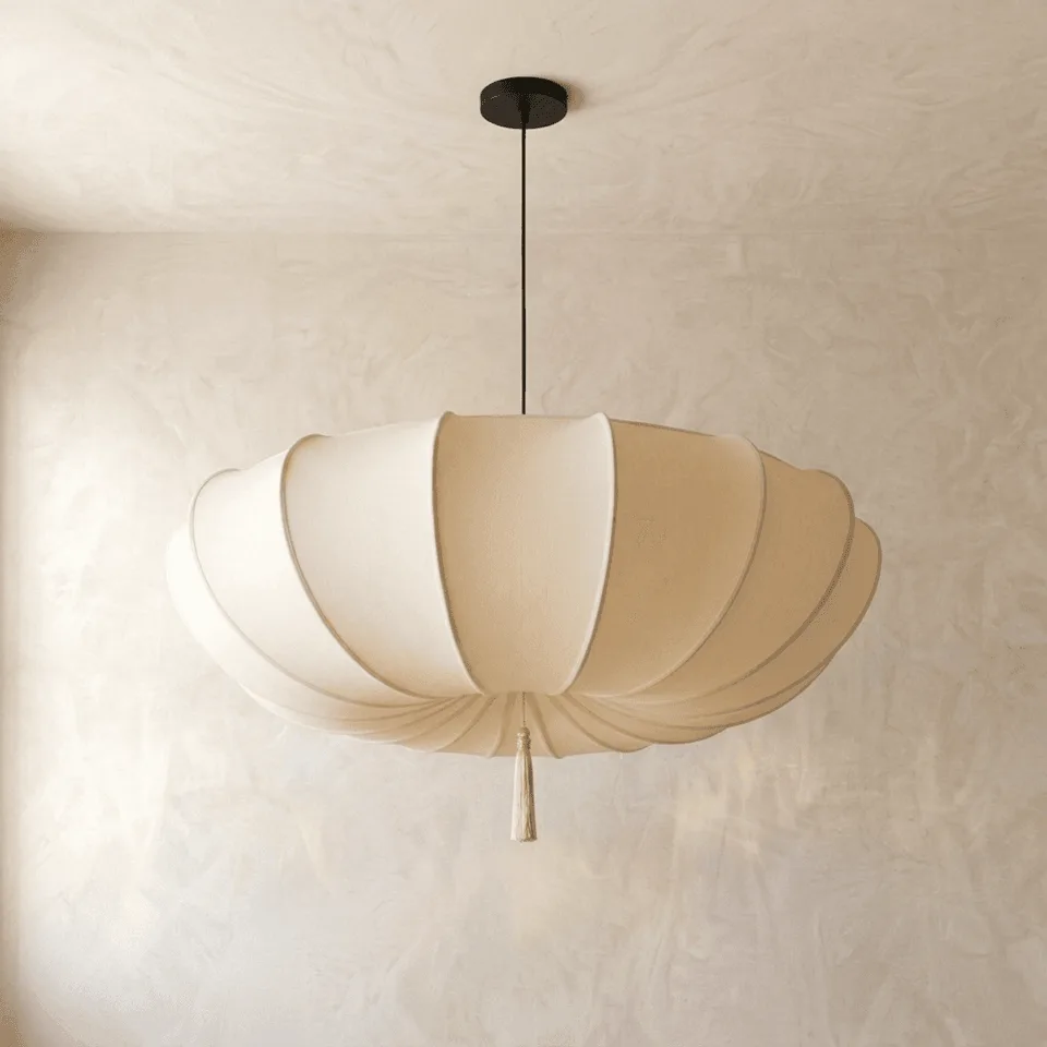 Scalloped silk pendant light with a cream pleated fabric shade and tassel, hanging on a plaster wall