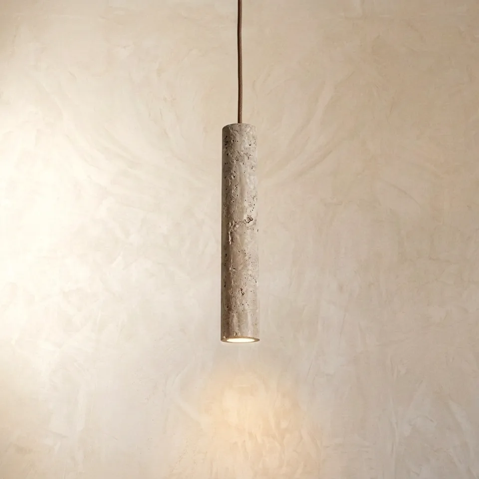 Natural travertine cylinder pendant light hanging against a plaster wall with a warm glow from the base