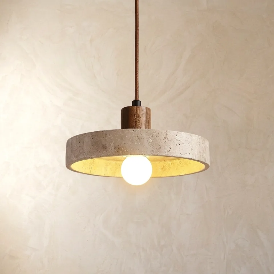 Travertine disc pendant light with a wood cap and frosted globe bulb glowing warmly against a plaster wall